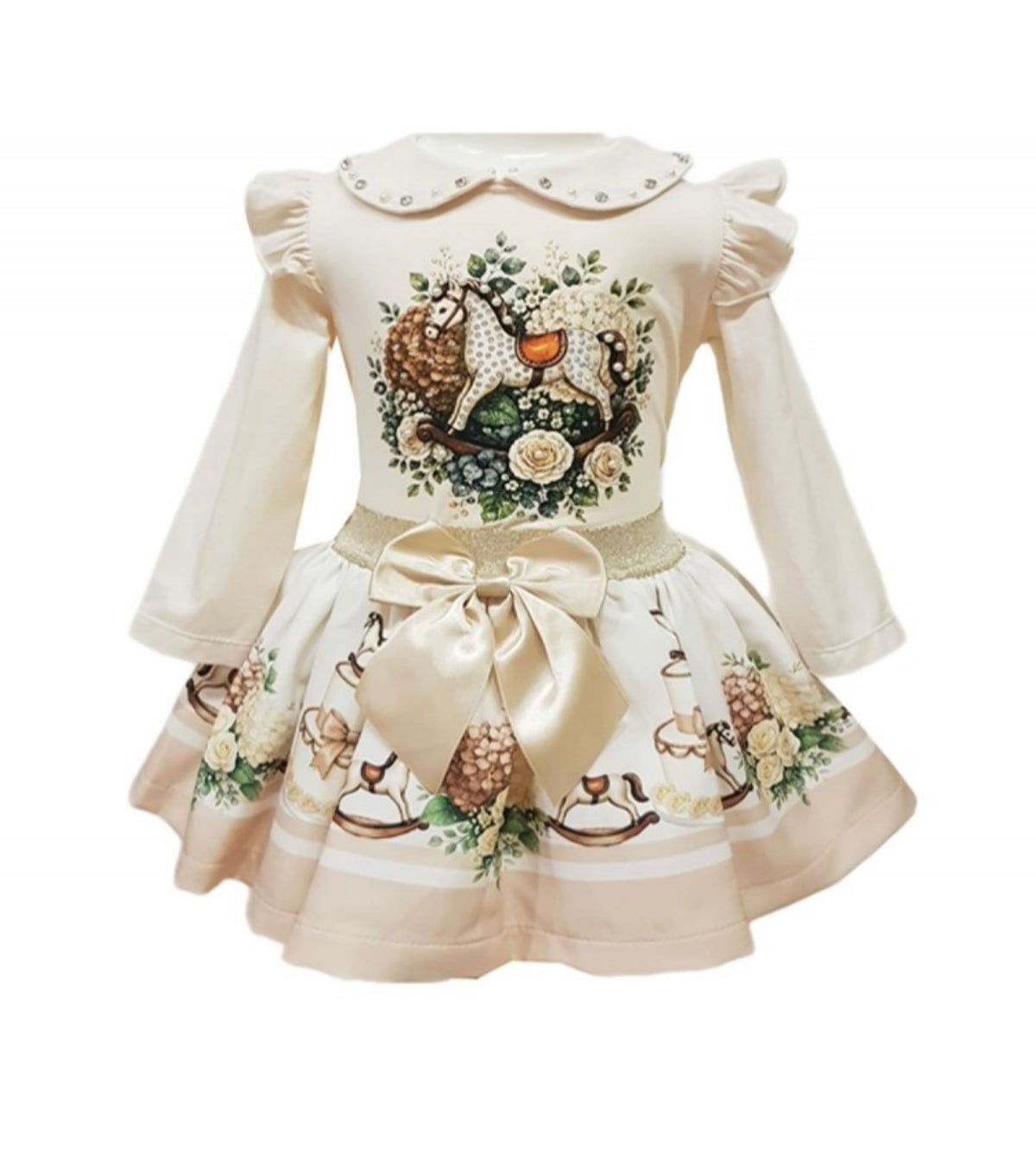 A long-sleeve baby dress in cream with a detailed woodland animal and floral print on the bodice and skirt, featuring a large satin bow at the waist and a decorative collar.