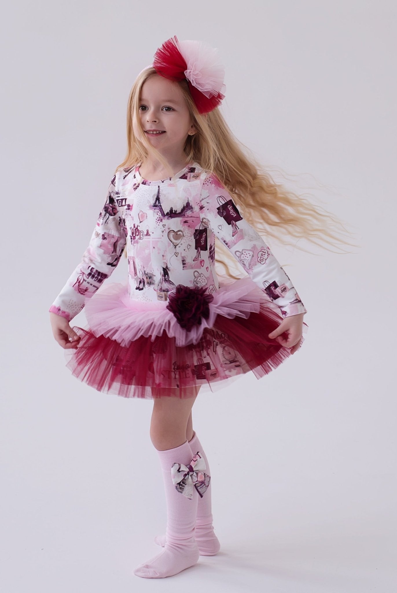 Young girl in a DAGA pink and burgundy printed tulle dress and pink tights on a white background