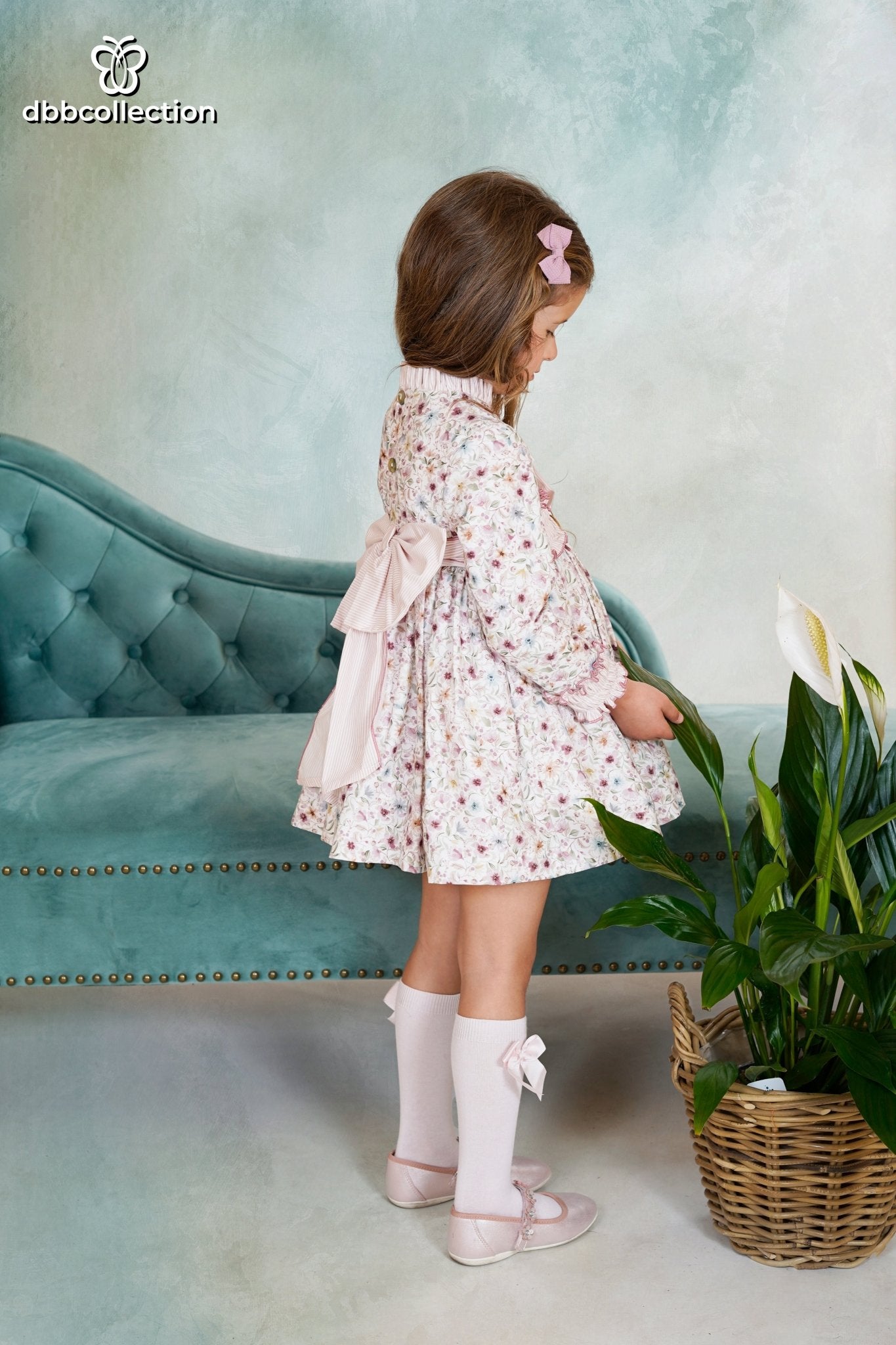 Girl wearing a long-sleeved floral dress with striped bow and ruffle trim from DBB Collection AW25, ages 4 to 10.