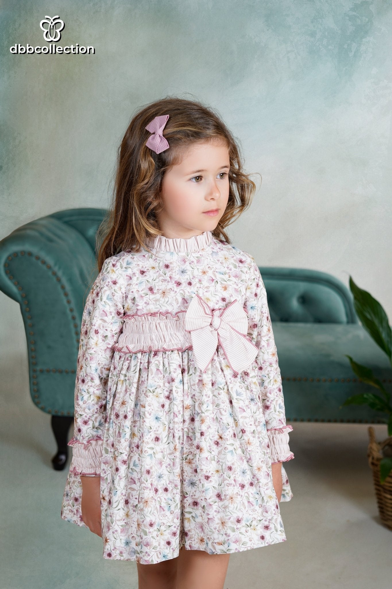 Girl wearing a long-sleeved floral dress with striped bow and ruffle trim from DBB Collection AW25, ages 4 to 10.
