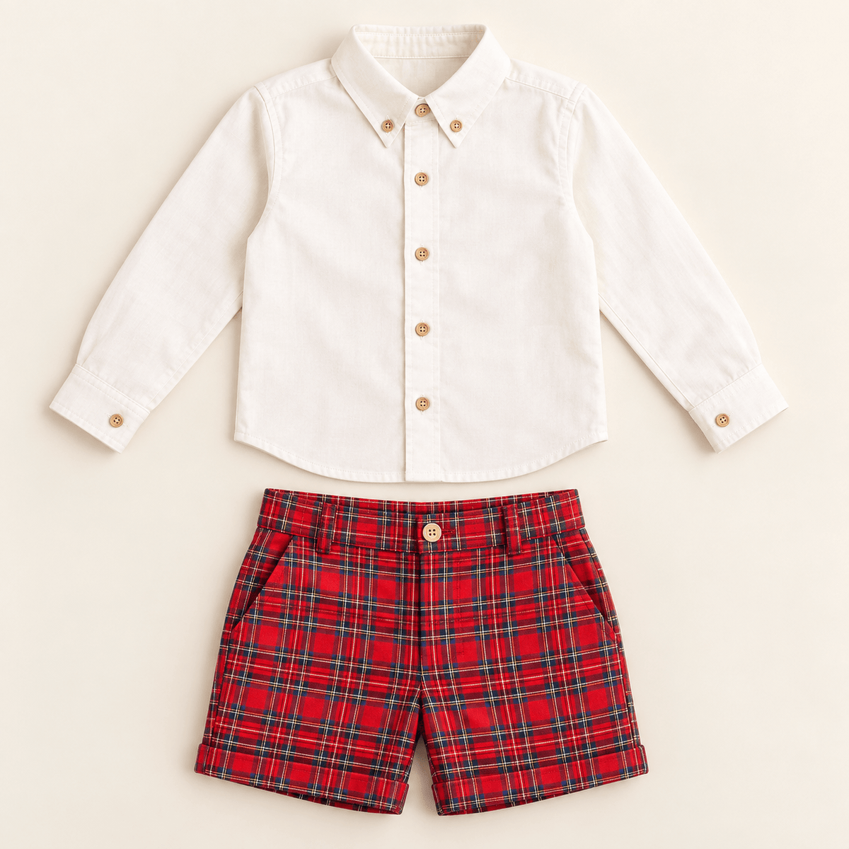 A toddler boy's two-piece outfit set featuring a white long-sleeve button-down shirt with gold buttons and red plaid shorts with green and black lines, laid flat on a light beige background.
