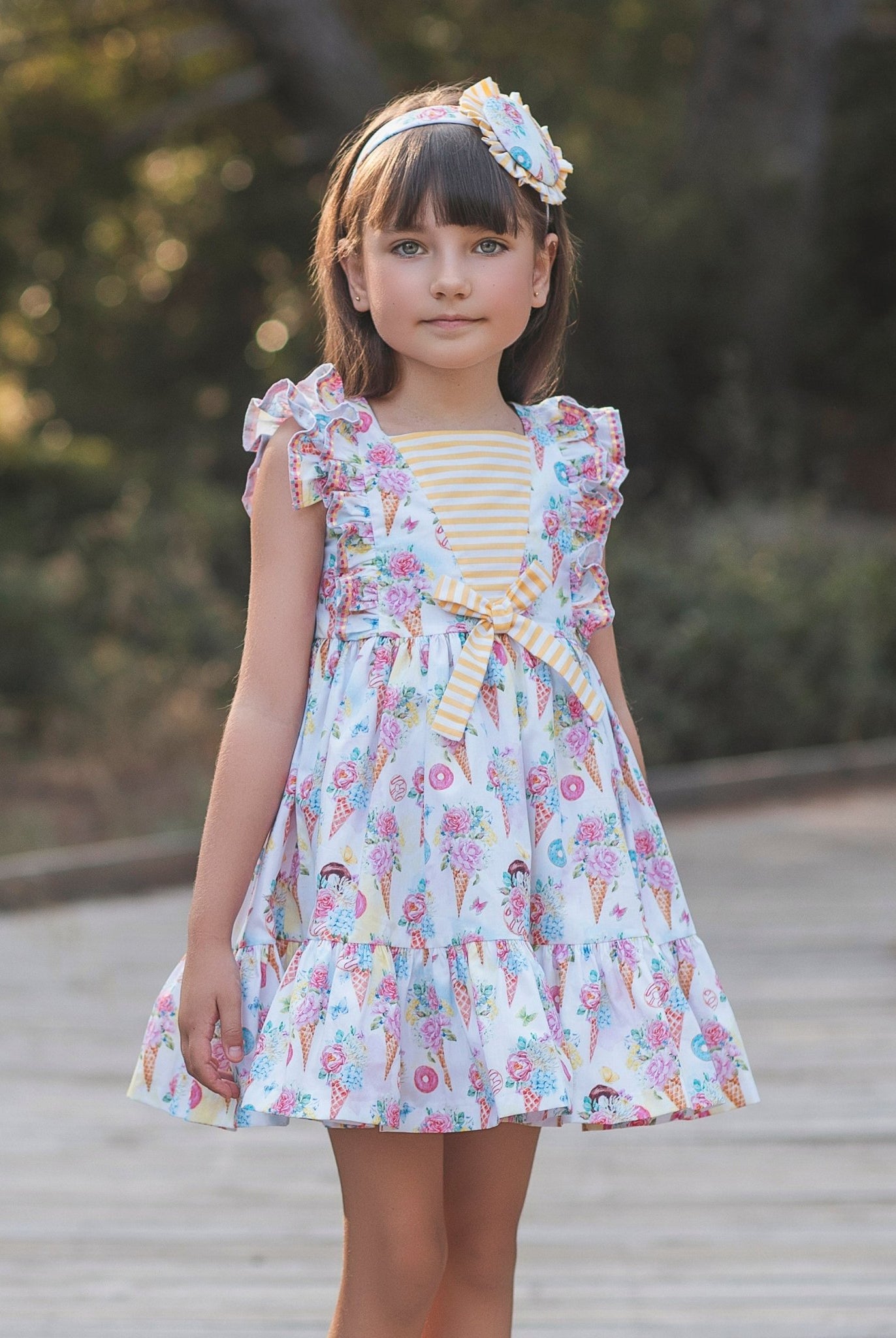 Young girl in Rochy SS26 Sweet Colletion Multicolour dress standing on a wooden path with trees in the background