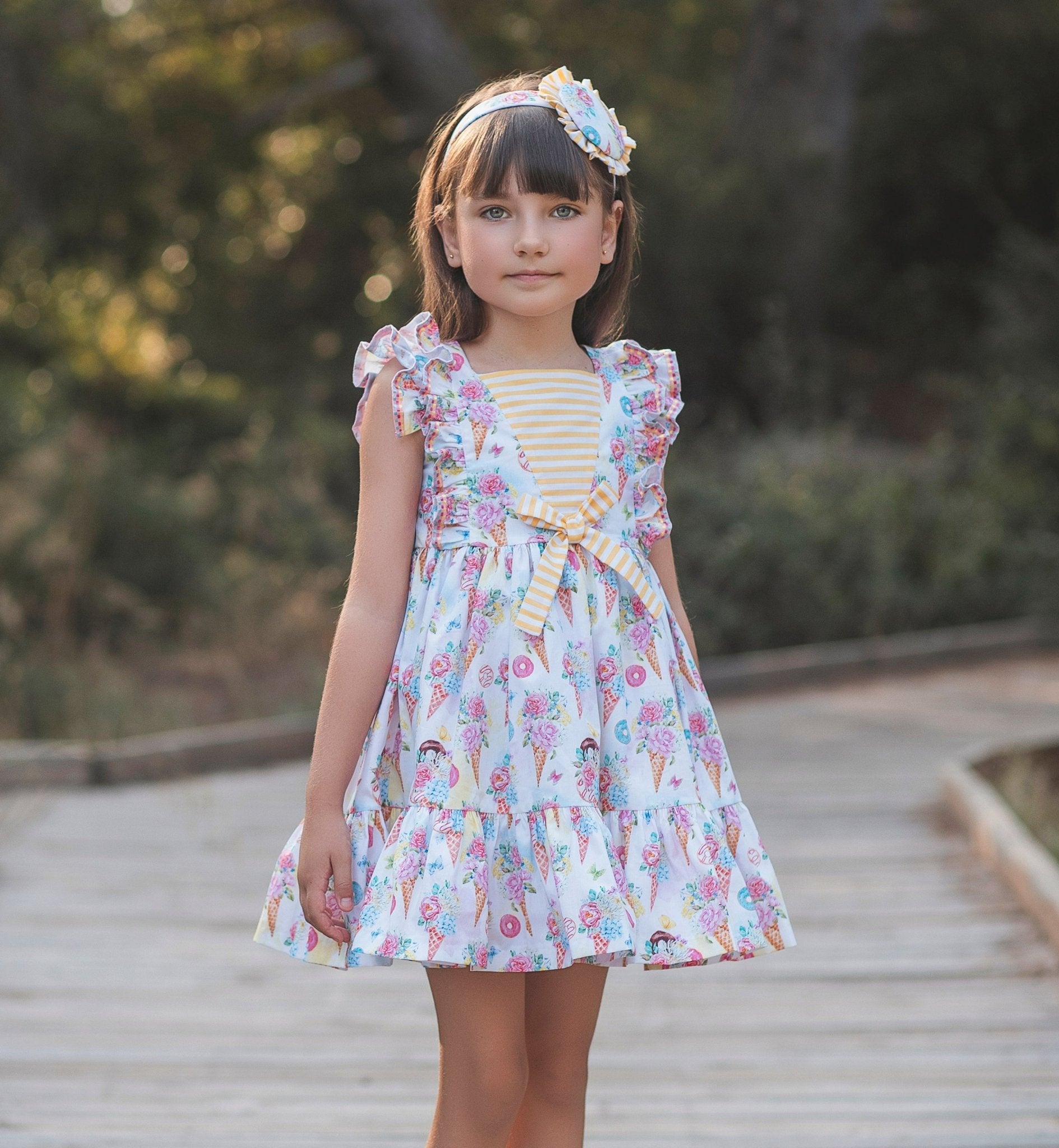 Young girl in Rochy SS26 Sweet Colletion Multicolour dress standing on a wooden path with trees in the background