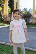 Naxos AW26 Girls Pink Tweed & Tulle Dress with matching hairbow worn by a young girl stood in a garden. 