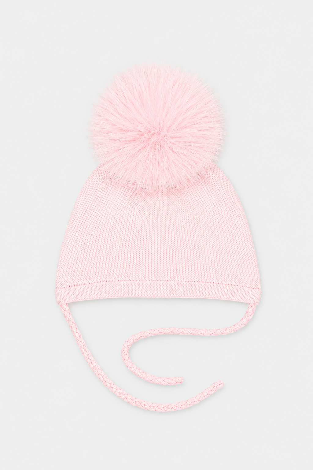 A light pink knit baby beanie hat with a fluffy pom-pom on top and matching tie strings, shown against a plain light gray background.