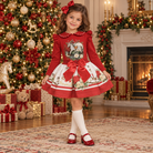 A young child wearing a red and cream rocking horse skirt and top set with peter pan collar and bow details in a beautiful Christmas decorated living room. 