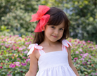 Child wearing Babine SS26 White and Neon Orange Trim Dress and matching hairbow. 