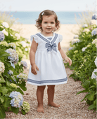 Baby Girl wearing a white and navy Summer dress with a beach and sea background. 