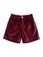 A pair of dark burgundy velvet shorts with pleats and a button closure, displayed flat against a solid white background.