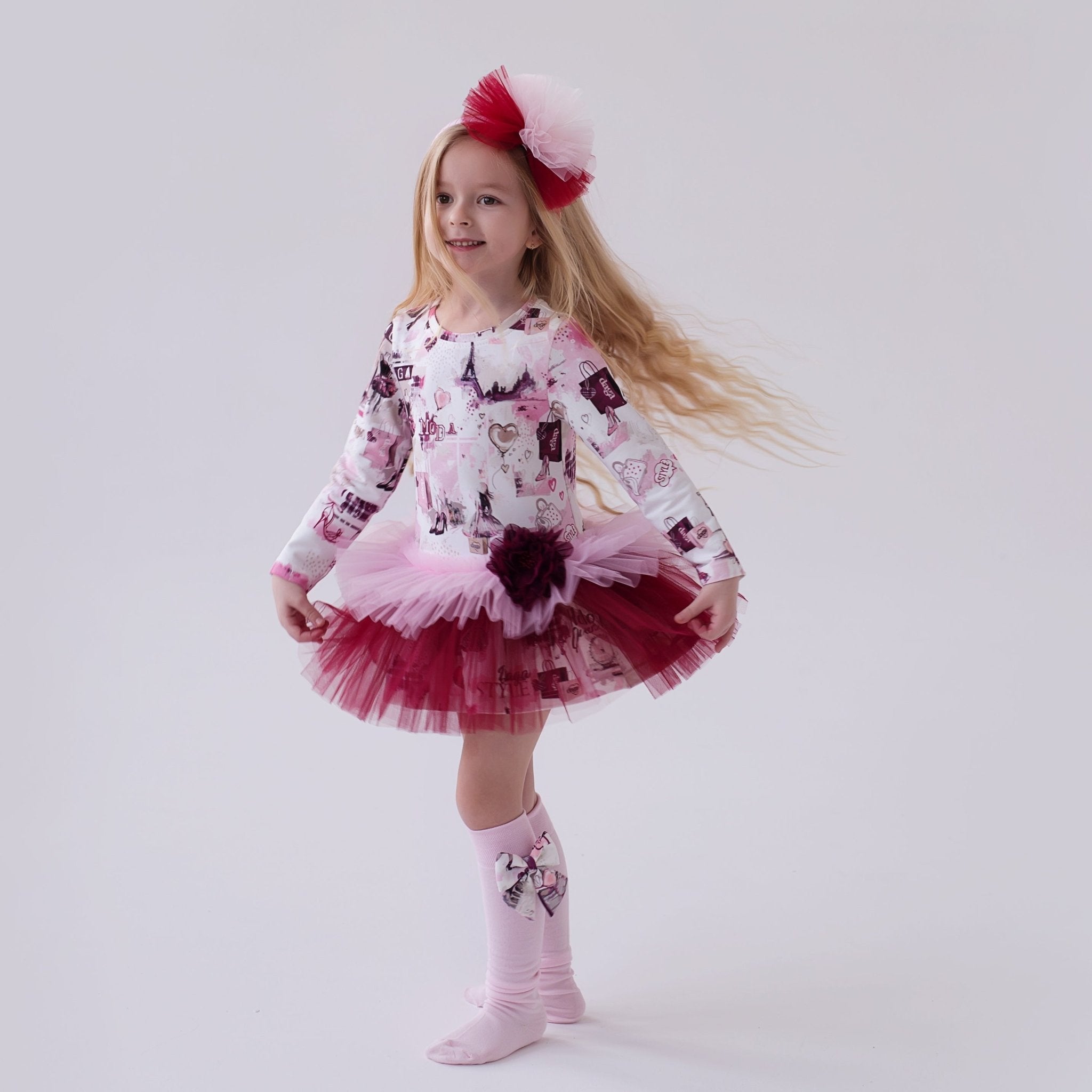 Young girl in a DAGA pink and burgundy printed tulle dress and pink tights on a white background