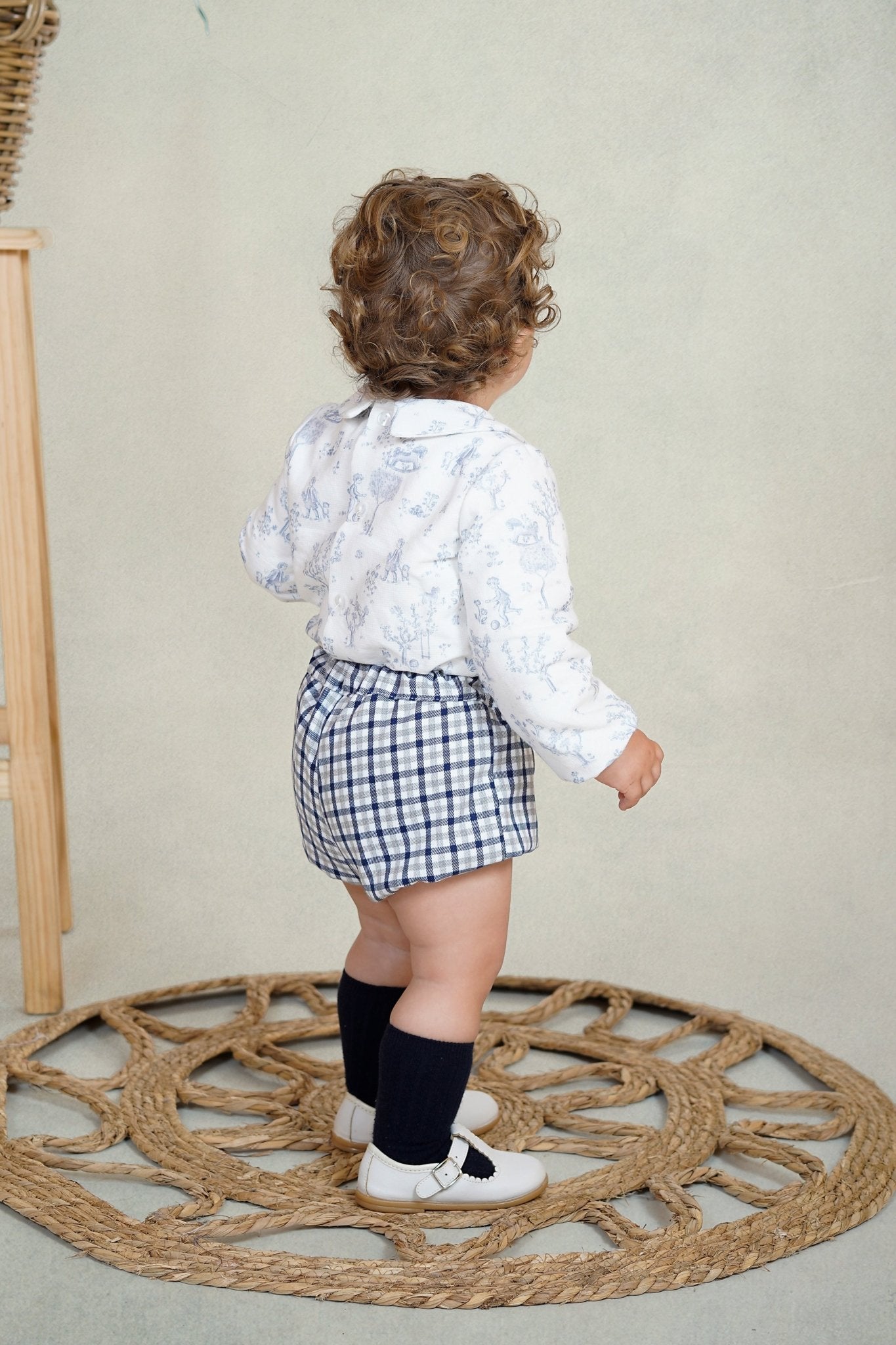 Baby boy wearing a blue woodland print shirt with Peter Pan collar and navy gingham shorts from DBB Collection AW25.