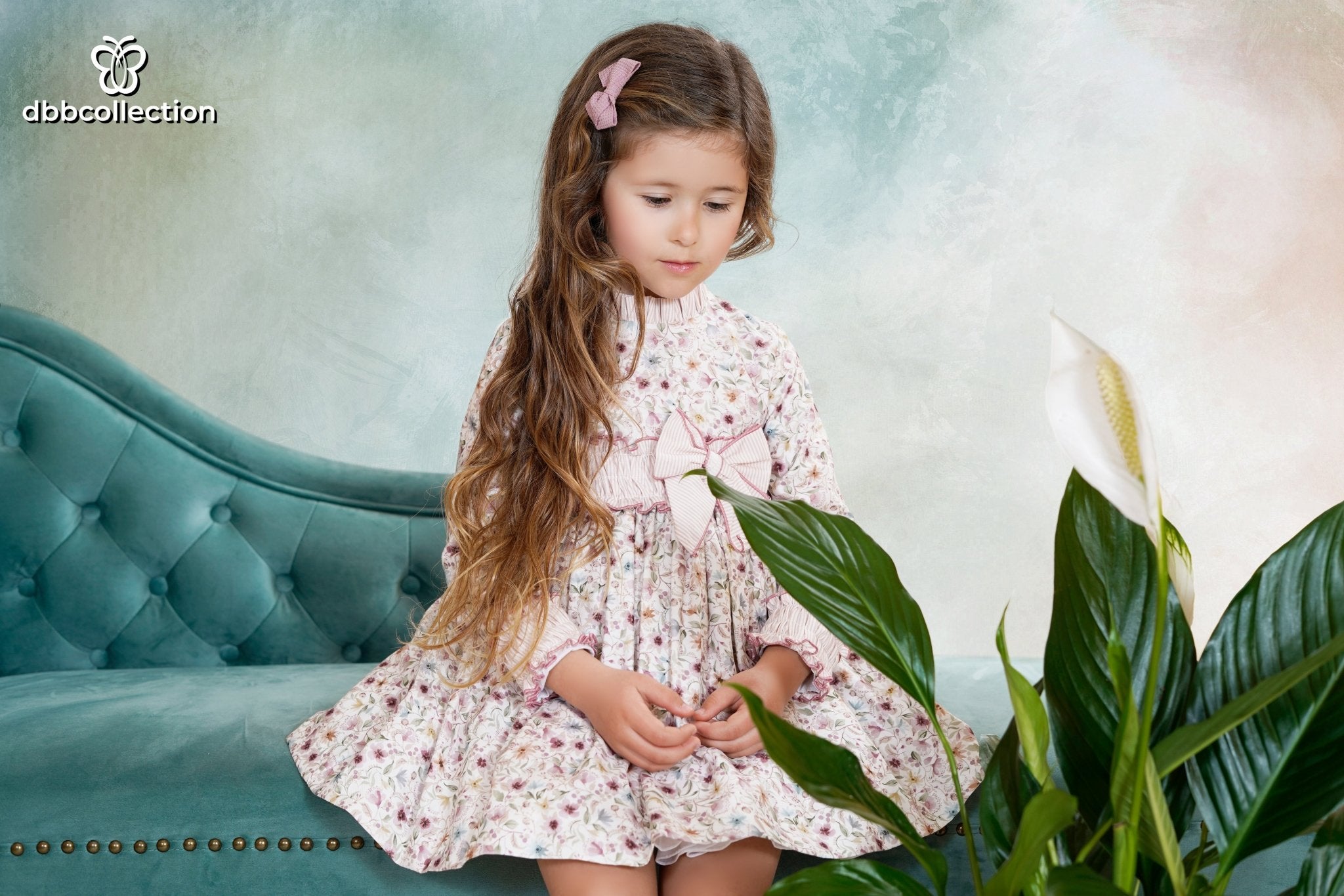 Girl wearing a long-sleeved floral dress with striped bow and ruffle trim from DBB Collection AW25, ages 4 to 10.