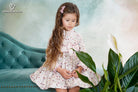 Girl wearing a long-sleeved floral dress with striped bow and ruffle trim from DBB Collection AW25, ages 4 to 10.