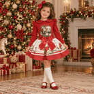 A young child wearing a red and cream rocking horse skirt and top set with peter pan collar and bow details in a beautiful Christmas decorated living room. 