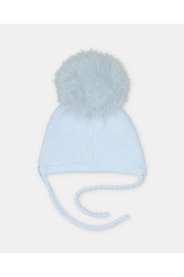 A light blue knit baby beanie hat with a fluffy pom-pom on top and braided ear ties, shown against a plain light gray background.