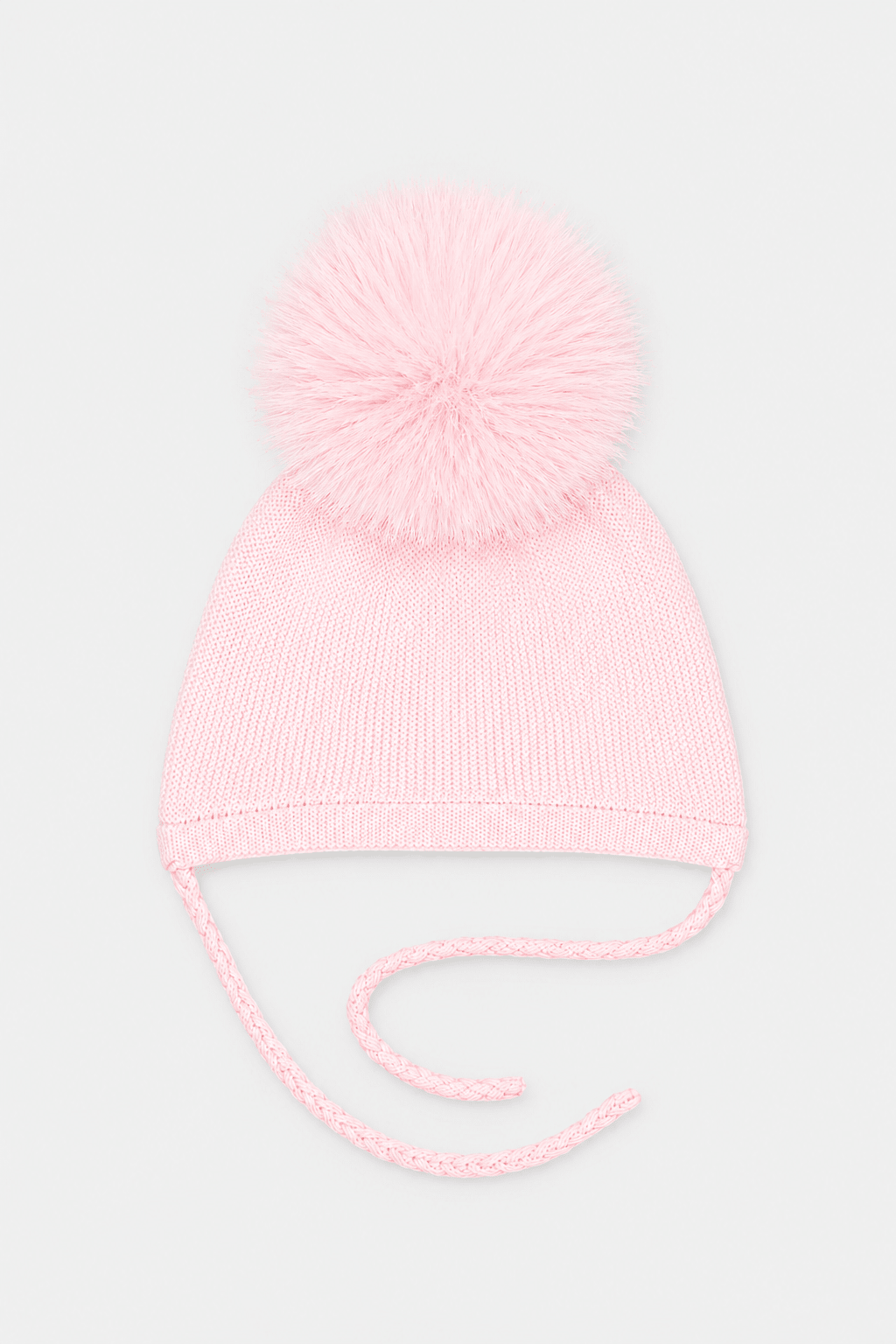 A light pink knit baby beanie hat with a fluffy pom-pom on top and matching tie strings, shown against a plain light gray background.