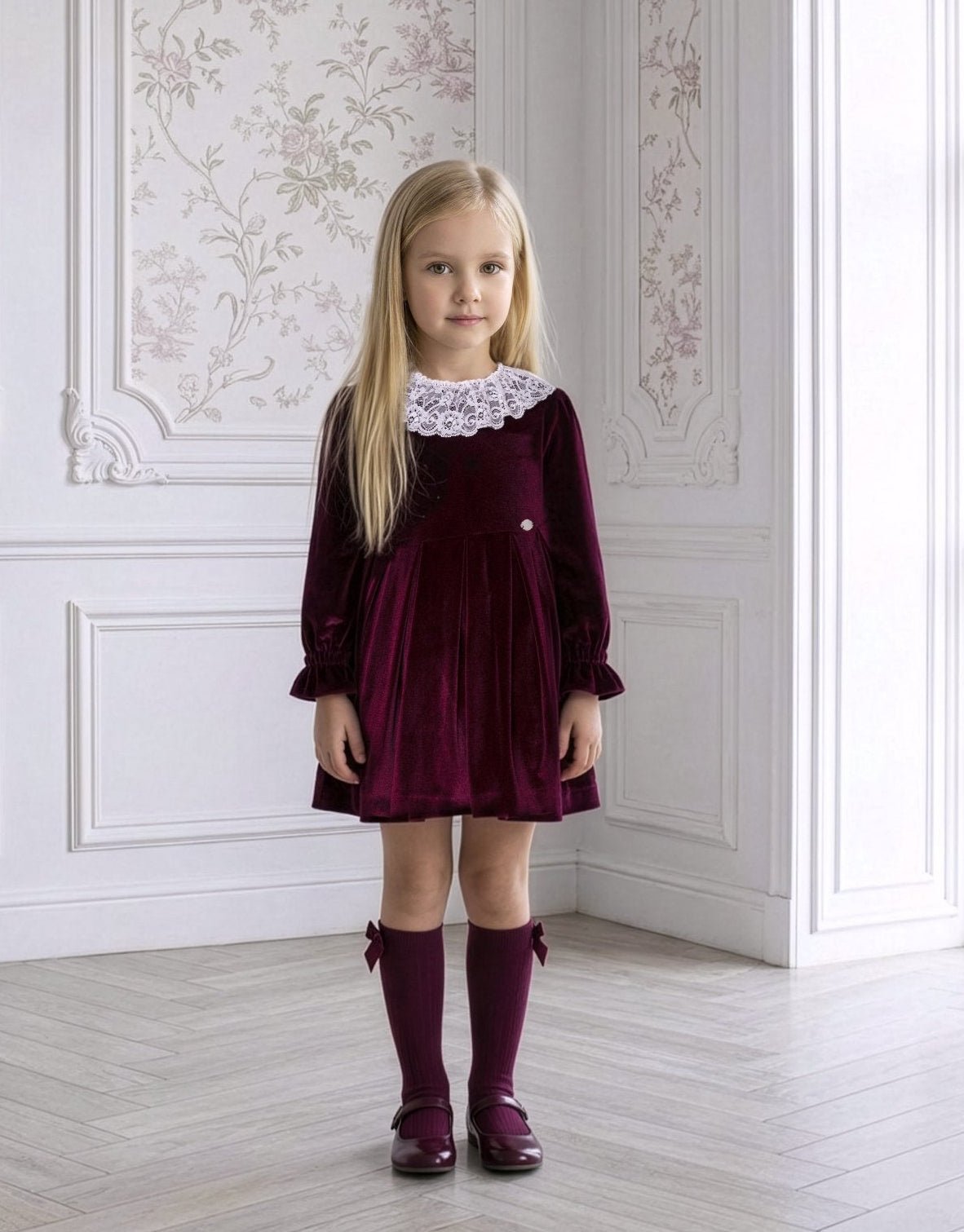 Young girl wearing Miranda AW26 burgundy dress with lace collar detail. 