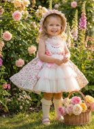 Young girl in a Sonata pink floral dress standing in a garden with flowers and a basket.