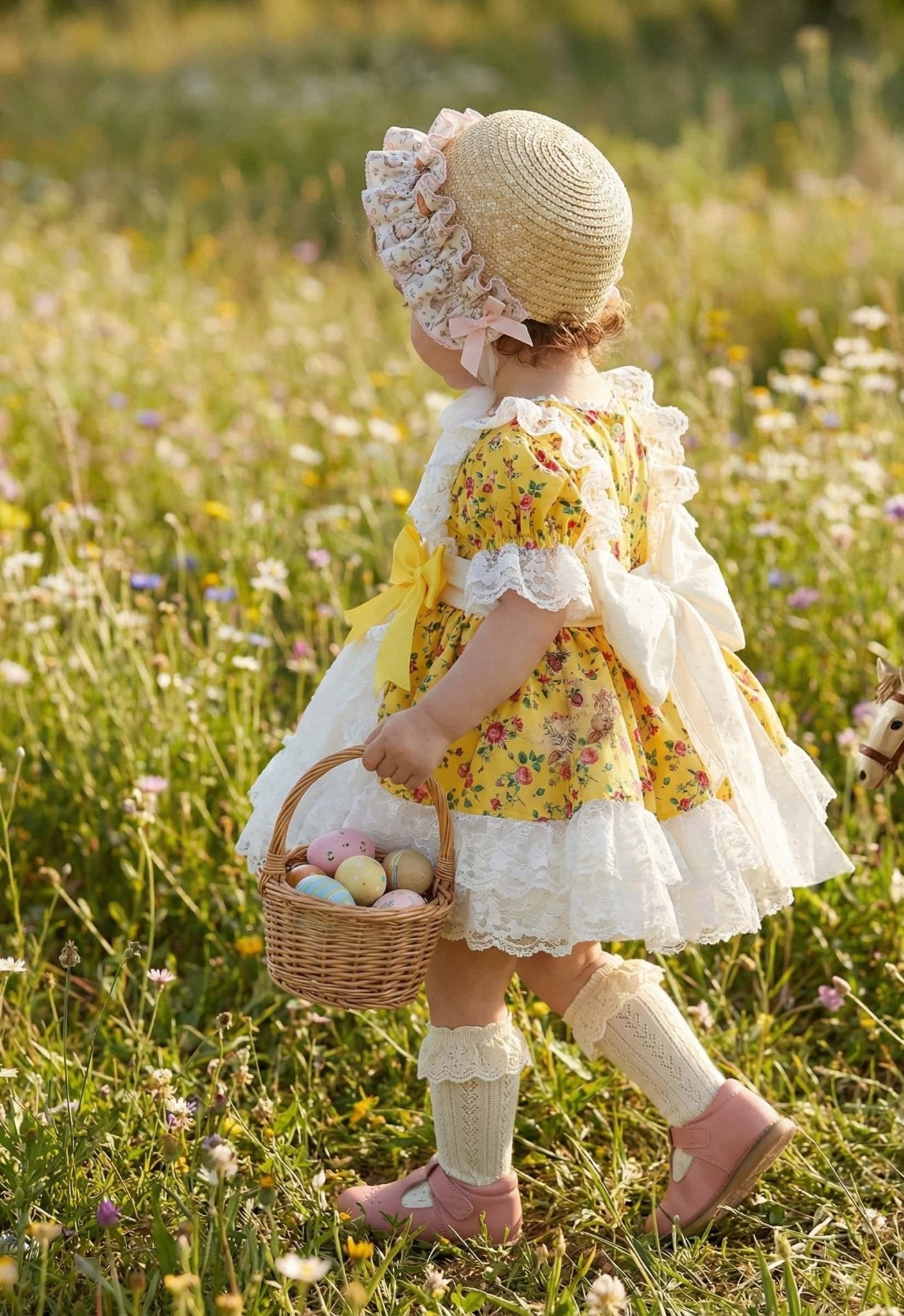 Child in a Sonata SS26 yellow dress with a basket of Easter eggs in a field of flowers