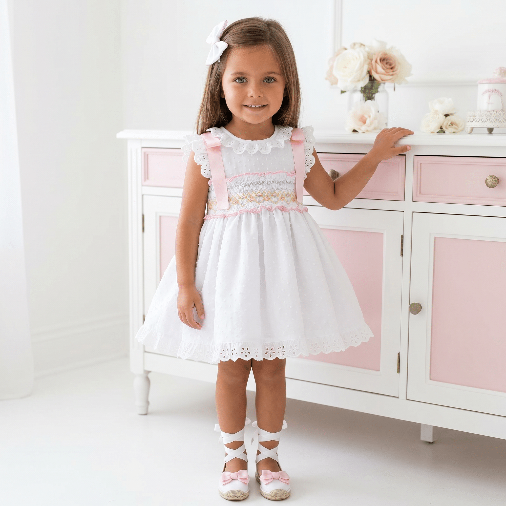 Sonata SS26 
Girls white smocked Spanish dress with pink ribbon detail, broderie anglaise trims and full skirt