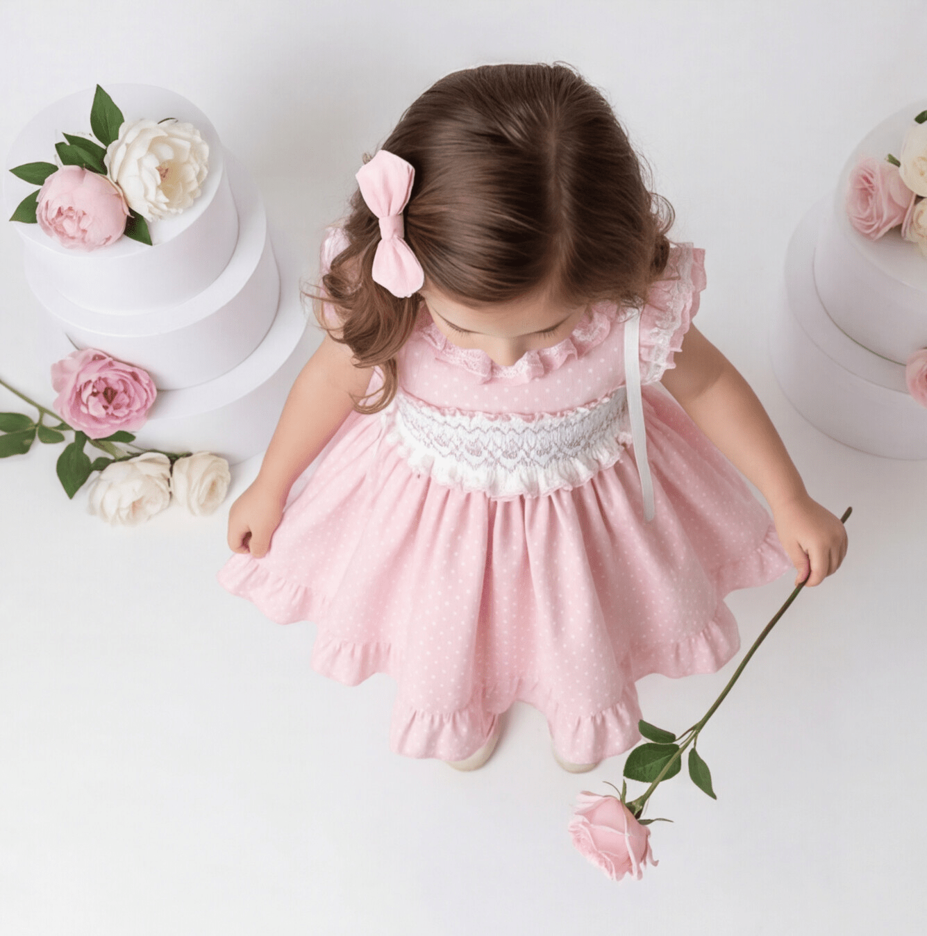 Child in a pink Sonata SMocked dress holding a flower with floral decorations in the background