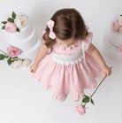 Child in a pink Sonata SMocked dress holding a flower with floral decorations in the background