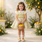Young girl in a yellow floral dress holding a basket of lemons in a lemon-themed setting.
